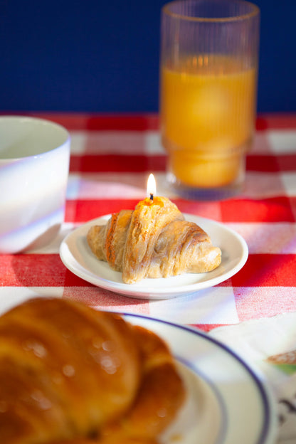 DOIY Duftkerze Croissant „Good Morning“ auf einem Frühstückstisch mit orangefarbener Saft und Kaffeetasse.