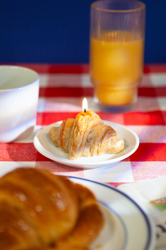 DOIY Duftkerze Croissant „Good Morning“ auf einem Frühstückstisch mit orangefarbener Saft und Kaffeetasse.
